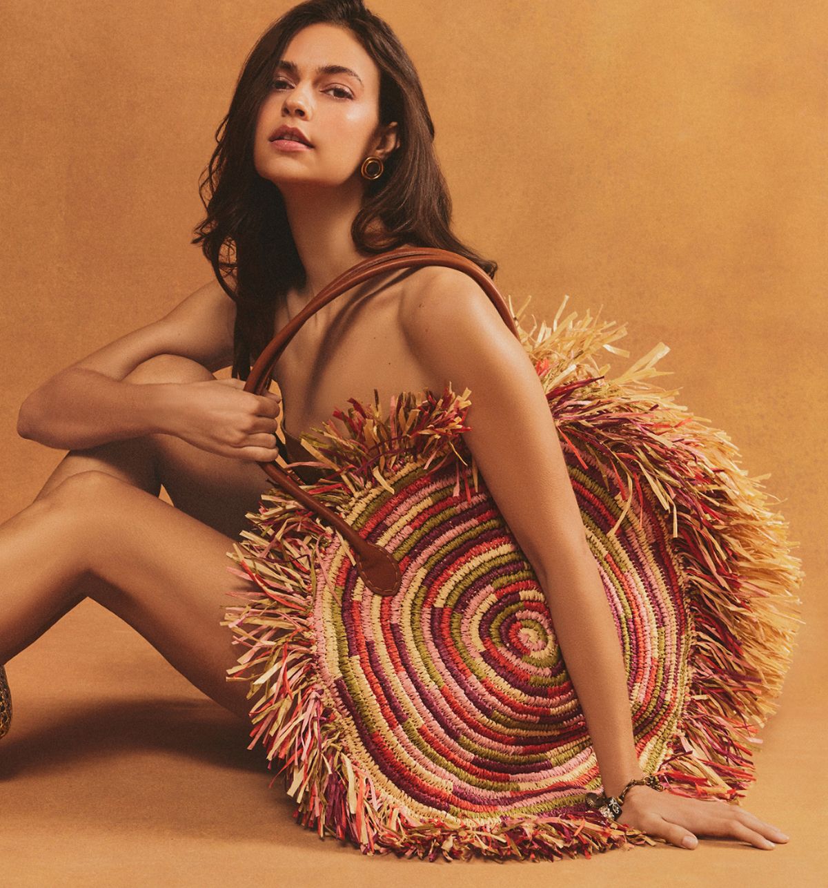 Seated model showcasing a large, multi-colored woven raffia Lily circular tote.