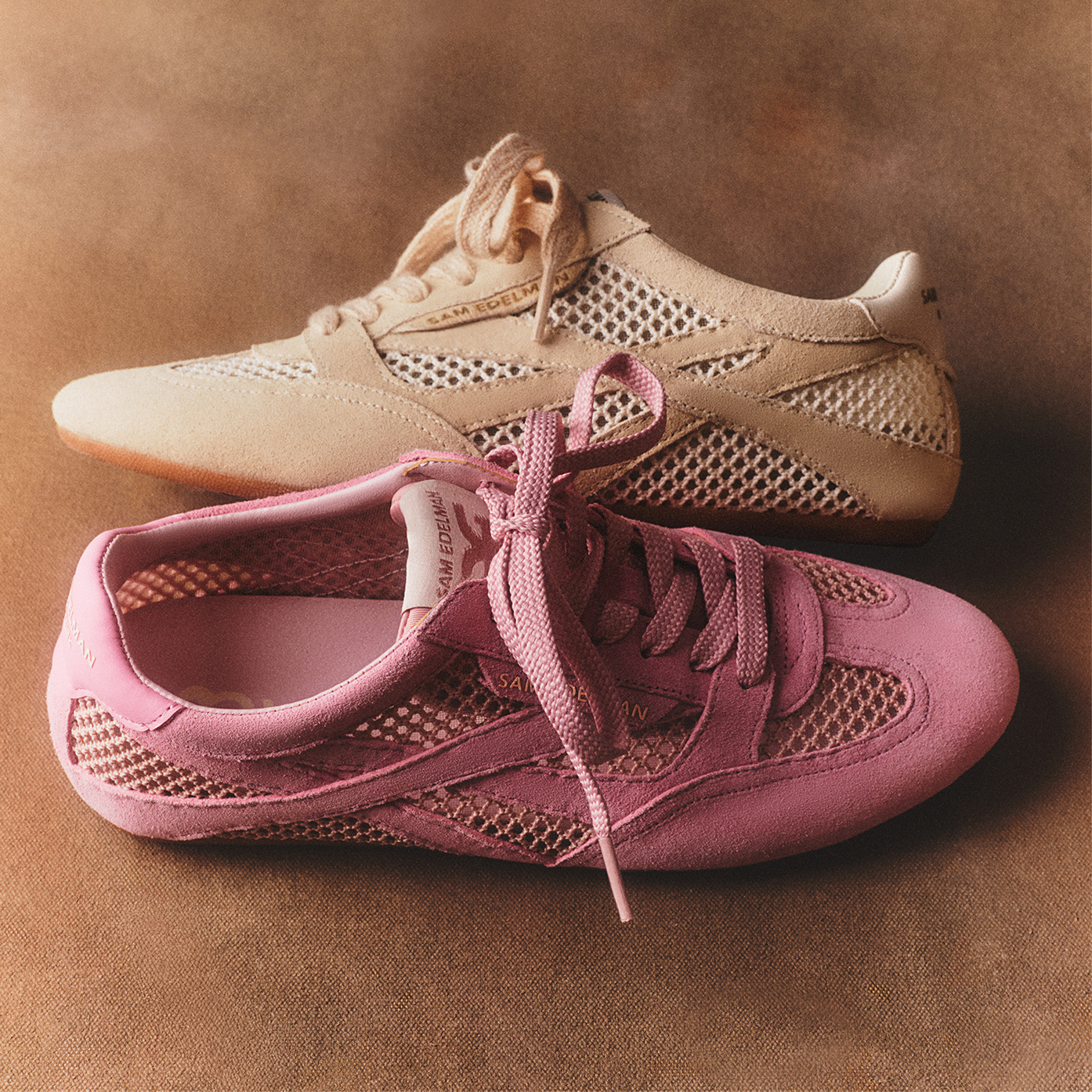 Two Sam Edelman Tobi lace-up sneakers with mesh and leather detailing in pink and cream against a tan backdrop.