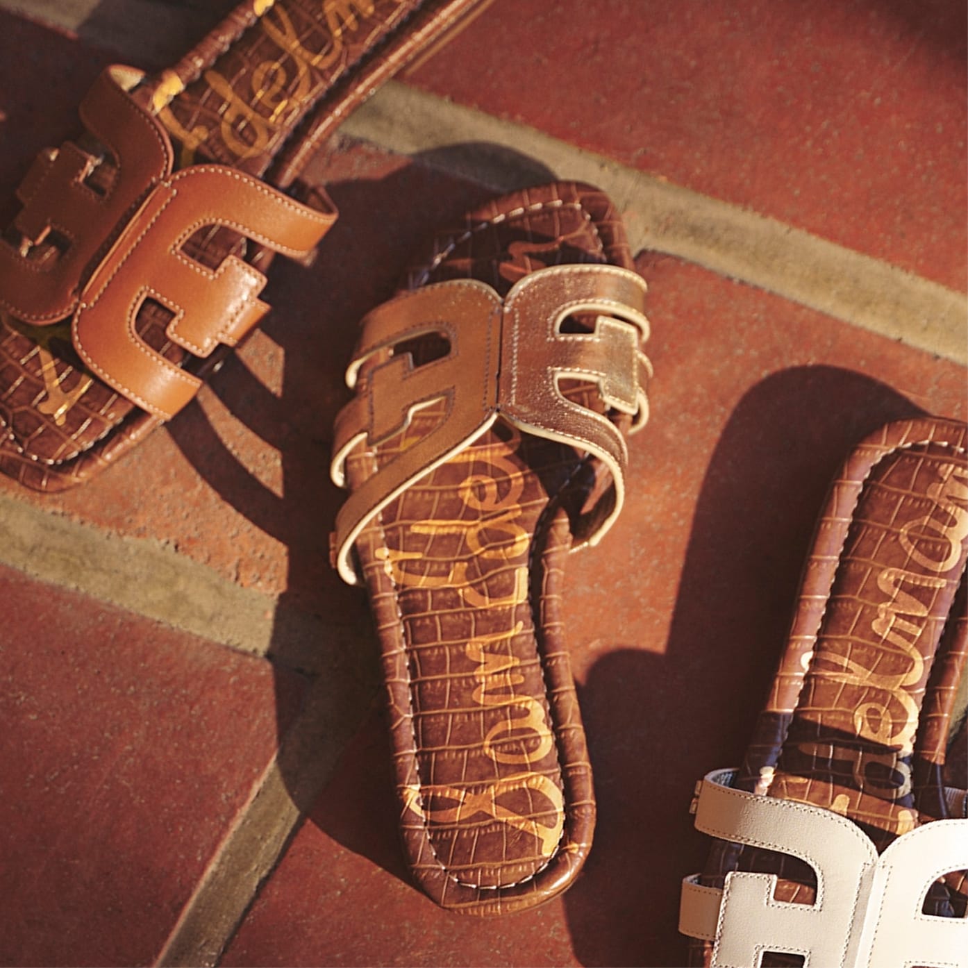 Sam Edelman Bay slide sandals with signature double-E strap detail in tan and ivory on terracotta tile